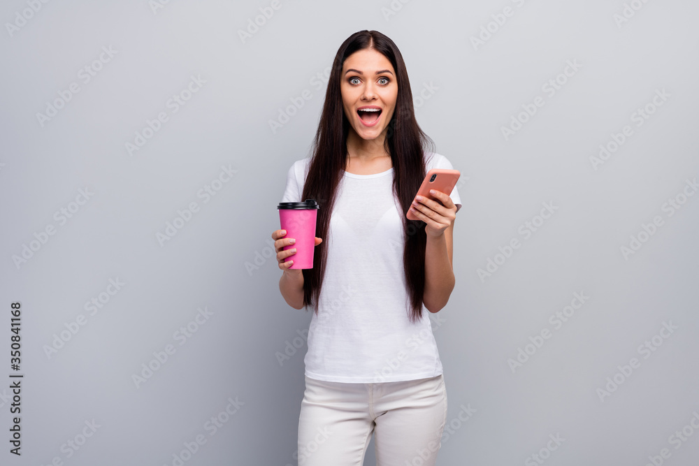 Portrait of her she nice attractive lovely lovable amazed cheerful straight-haired girl holding in hands using cell drinking latte having fun isolated over light gray pastel color background Portrait of her she nice attractive lovely lovable amazed cheerful straight-haired girl holding in hands using cell drinking latte having fun isolated over light gray pastel color background