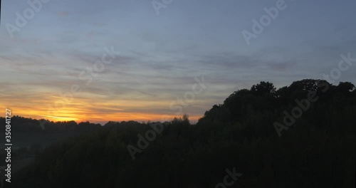Fast aerial movement through canopy of trees to reveal sunset and huge rolling hill landscape