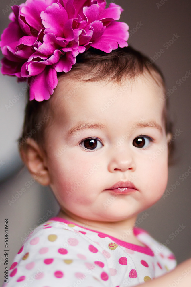 Adorable sweet baby girl with big pink flower on head, closeup portrait of cute girl, beautiful toddler Adorable sweet baby girl with big pink flower on head, closeup portrait of cute girl, beautiful toddler