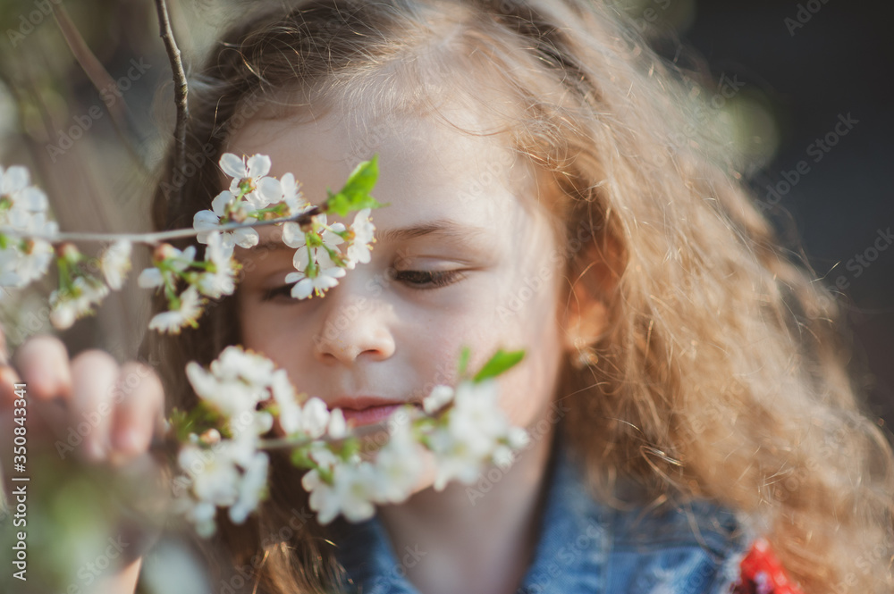Cute little girl with curly hair in a flowering garden