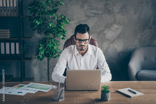 Portrait of his he nice attractive focused director writing email preparing creating presentation launching start-up project IT geek at modern loft industrial style interior work place station indoors