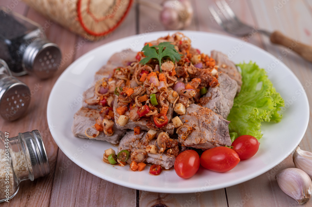 Spicy pork minced with tomatoes and lettuce on a white plate on a wooden table. Spicy pork minced with tomatoes and lettuce on a white plate on a wooden table.