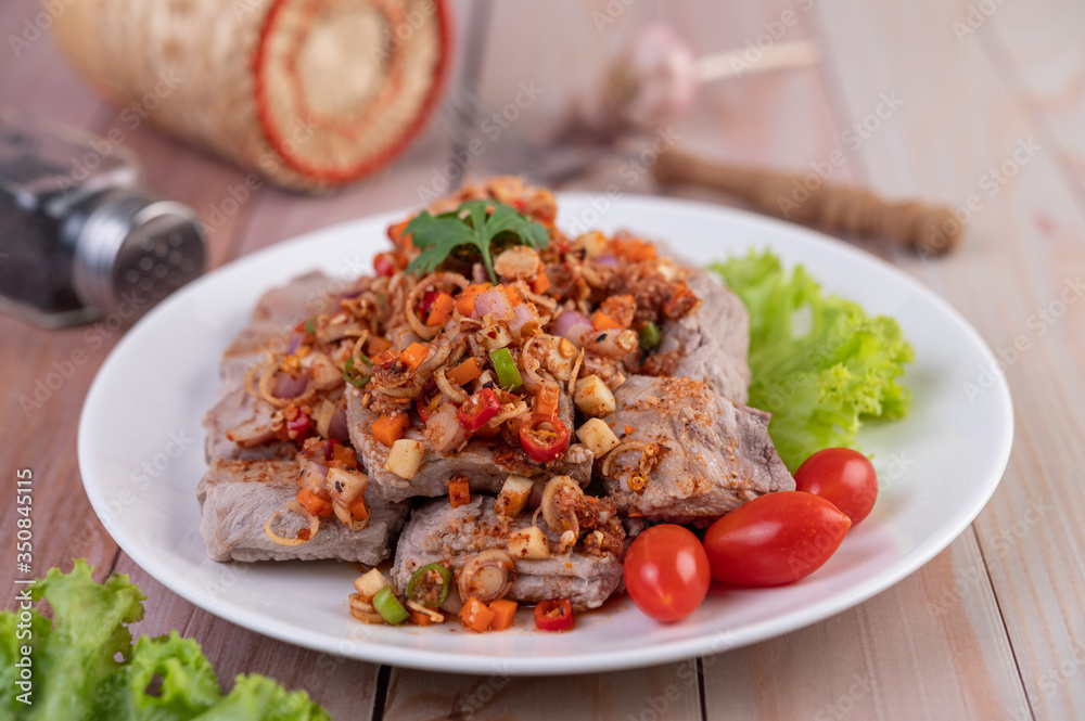 Spicy pork minced with tomatoes and lettuce on a white plate on a wooden table. Spicy pork minced with tomatoes and lettuce on a white plate on a wooden table.
