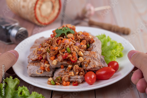 Spicy pork minced with tomatoes and lettuce on a white plate on a wooden table.