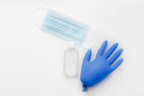 A blue rubber glove with air inside lies on a light background next to a medical disposable protective mask and hand antiseptic in a transparent bottle - virus protection