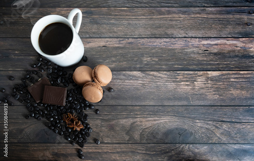 wooden background with coffee cup, coffee beans, star anise, chocolate and coffee macarons. Top view