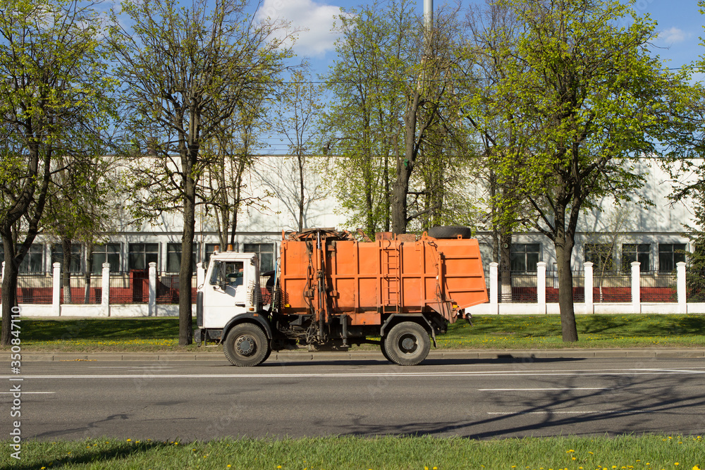 An orange garbage truck rides along a city street
