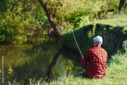 Fisher man fishing with spinning rod on a river bank, spin fishing, prey fishing © Serhii