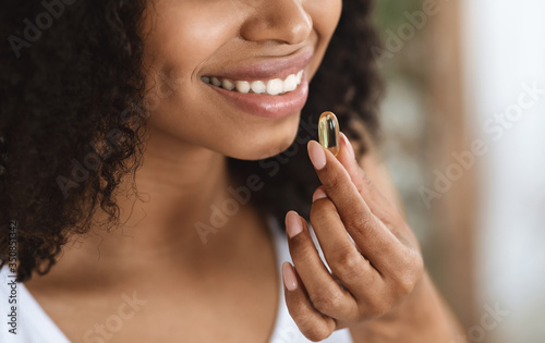 Beauty Supplement. Closeup Of Smiling Black Woman Taking Vitamin Pill Capsule photo
