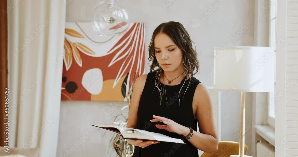 Young woman reading book in her apartment, looking at camera with smile. Young woman reading book in her apartment, looking at camera with smile.