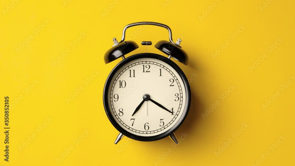 Time on vintage black alarm clock running from 7.00 to 8.00 isolated on yellow background color. One hour time lapse of black alarm clock running from 7.00 to 8.00.