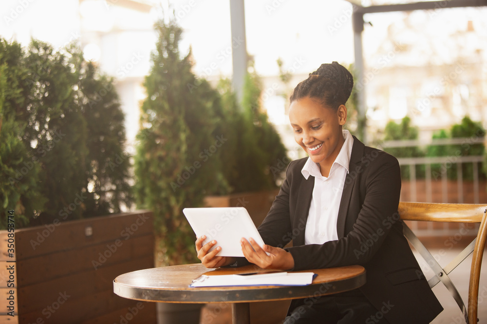 Using tablet, videocall. African-american businesswoman in office attire smiling, looks confident happy, busy. Finance, business, equality and human rights concept. Beautiful young model, successful. Using tablet, videocall. African-american businesswoman in office attire smiling, looks confident happy, busy. Finance, business, equality and human rights concept. Beautiful young model, successful.