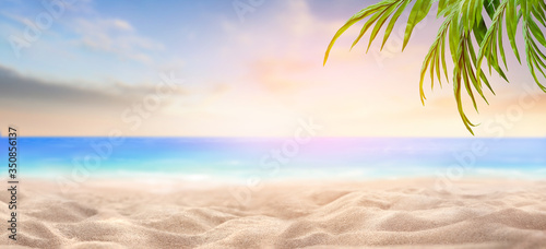 Fototapeta Naklejka Na Ścianę i Meble -  A summer vacation, holiday background of a tropical beach and blue sea at sunset with green palm tree leaves.