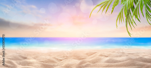 A summer vacation, holiday background of a tropical beach and blue sea at sunset, sun flare bokeh and green palm tree leaves.