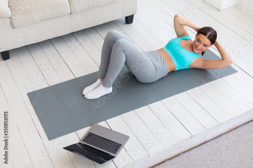 Fit Girl Doing Abs Exercise Training At Laptop Indoors, High-Angle