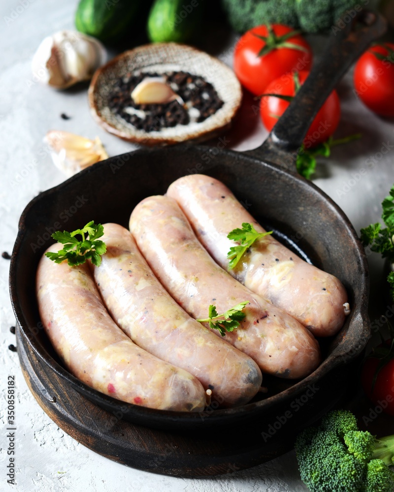 Raw homemade sausages (chicken, turkey) in a pan on a gray background with vegetables. Still life Raw homemade sausages (chicken, turkey) in a pan on a gray background with vegetables. Still life