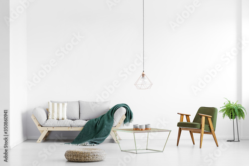 Real photo of a simple living room interior with a sofa, pouf and armchair
