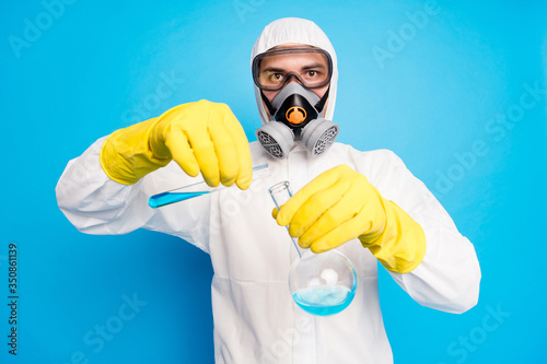 Portrait of smart scientist pour ncov vaccination probe wear white suit hazmat yellow latex gloves goggles breathing mask isolated over blue color background