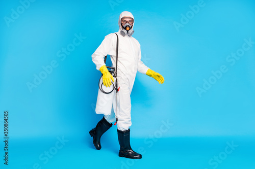 Full body photo of medical worker man go walk clean home house disinfect covid pathogen infection wear hazmat gas mask protective glasses gloves boots isolated blue color background