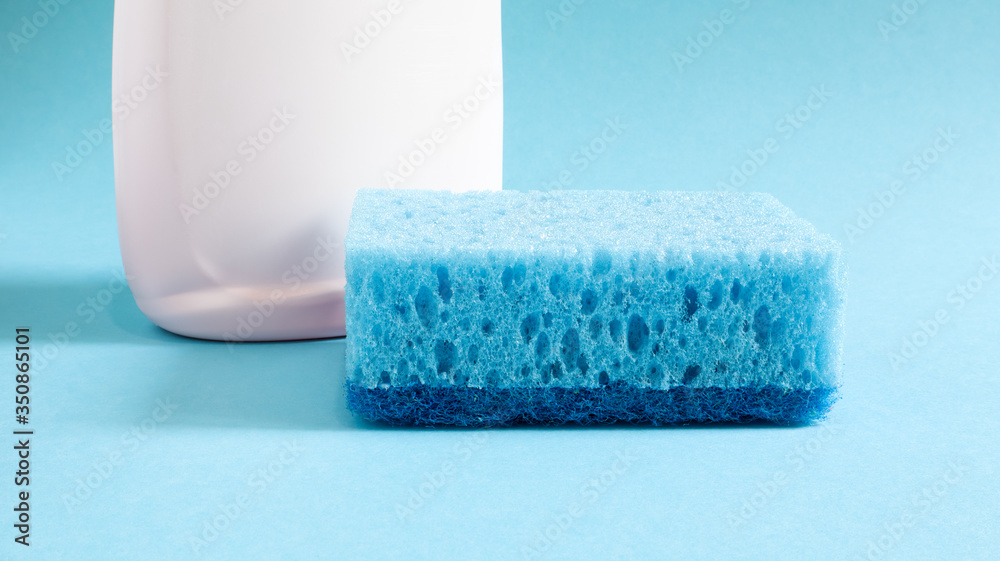 One blue sponge with a white bottle of detergent on a blue background. Convenience of sponges consists in good detergent retention that allows to use it economically One blue sponge with a white bottle of detergent on a blue background. Convenience of sponges consists in good detergent retention that allows to use it economically