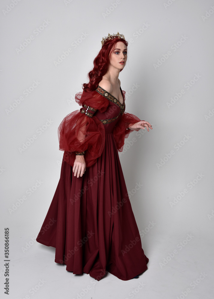 Portrait of a beautiful woman with red hair wearing a flowing Burgundy fantasy gown and golden crown. full length standing pose, isolated against a studio background
Portrait of a beautiful woman with red hair wearing a flowing Burgundy fantasy gown and golden crown. full length standing pose, isolated against a studio background