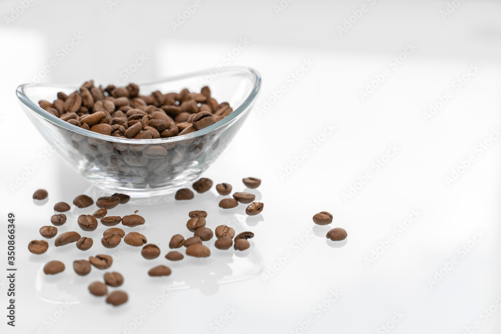 Coffee beans in a glass bowl on a glossy light table. some grains are scattered on the table. breakfast concept Coffee beans in a glass bowl on a glossy light table. some grains are scattered on the table. breakfast concept