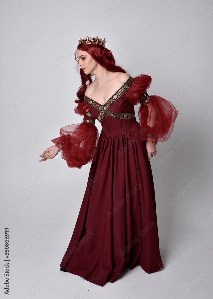 Portrait of a beautiful woman with red hair wearing a flowing Burgundy fantasy gown and golden crown. full length standing pose, isolated against a studio background
Portrait of a beautiful woman with red hair wearing a flowing Burgundy fantasy gown and golden crown. full length standing pose, isolated against a studio background