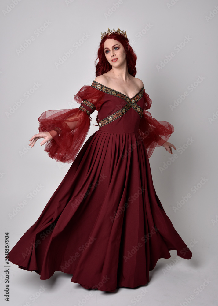 Portrait of a beautiful woman with red hair wearing a flowing Burgundy fantasy gown and golden crown. full length standing pose, isolated against a studio background
Portrait of a beautiful woman with red hair wearing a flowing Burgundy fantasy gown and golden crown. full length standing pose, isolated against a studio background
