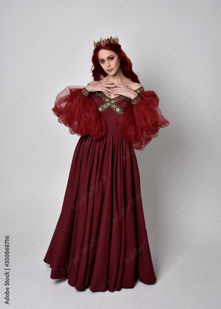 Portrait of a beautiful woman with red hair wearing a flowing Burgundy fantasy gown and golden crown. full length standing pose, isolated against a studio background
Portrait of a beautiful woman with red hair wearing a flowing Burgundy fantasy gown and golden crown. full length standing pose, isolated against a studio background