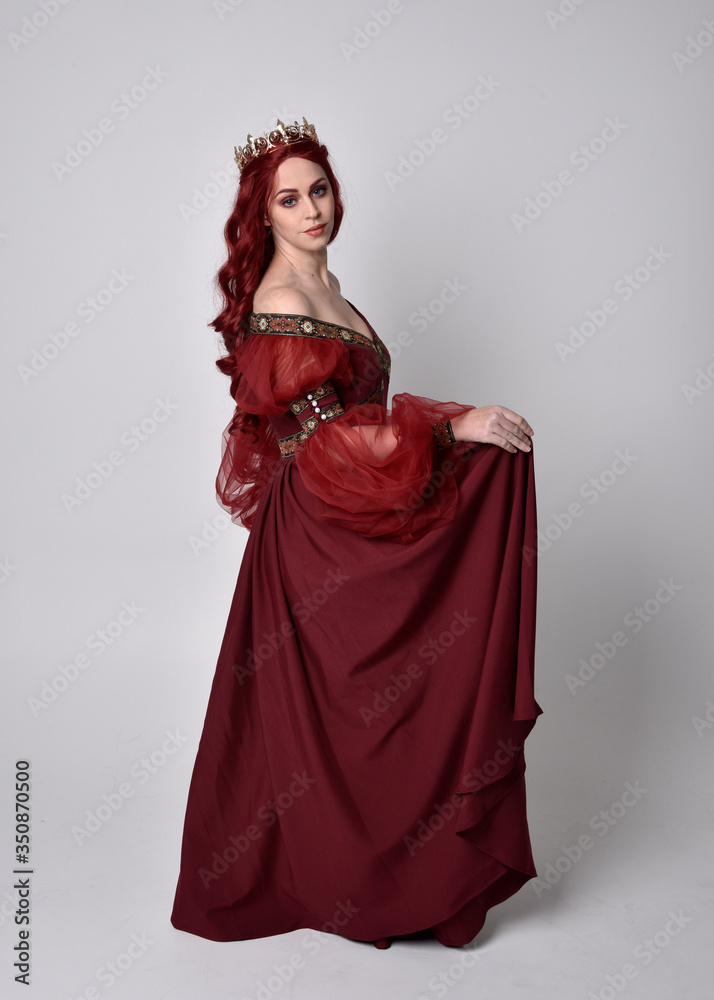 Portrait of a beautiful woman with red hair wearing a flowing Burgundy fantasy gown and golden crown. full length standing pose, isolated against a studio background
Portrait of a beautiful woman with red hair wearing a flowing Burgundy fantasy gown and golden crown. full length standing pose, isolated against a studio background