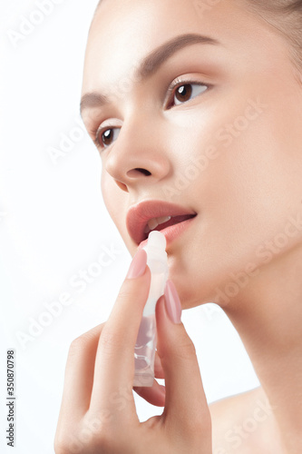 Young beautiful woman with clean perfect skin inflicts balm on lips