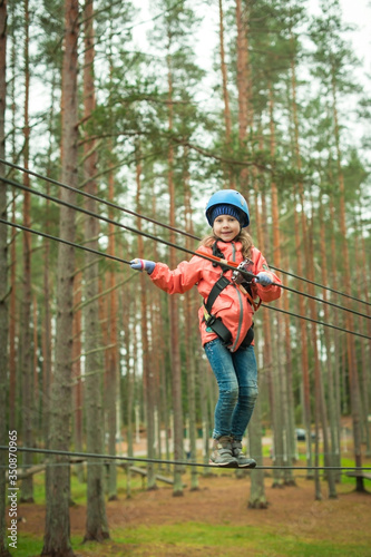 a girl walks on a tightrope to a rope park, a climbing center. Hiking in the rope park, the girls are safe.