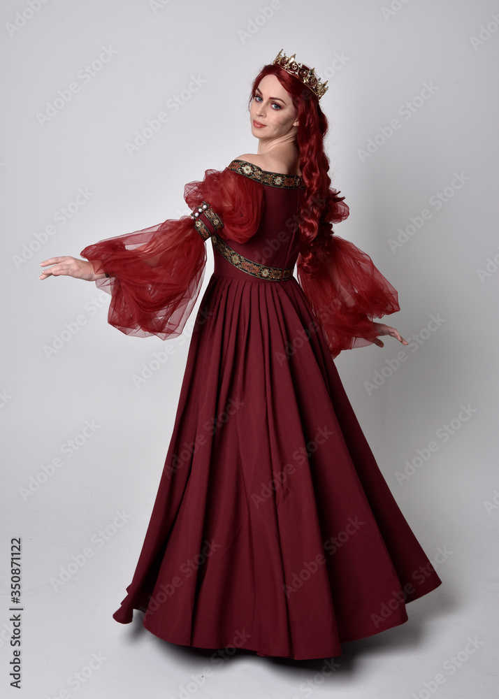 Portrait of a beautiful woman with red hair wearing a flowing Burgundy fantasy gown and golden crown. full length standing pose, isolated against a studio background
Portrait of a beautiful woman with red hair wearing a flowing Burgundy fantasy gown and golden crown. full length standing pose, isolated against a studio background
