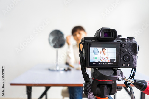 Young female blogger reviewing and recording vlog video on camera screen with makeup cosmetic at home. Focus on camera screen.