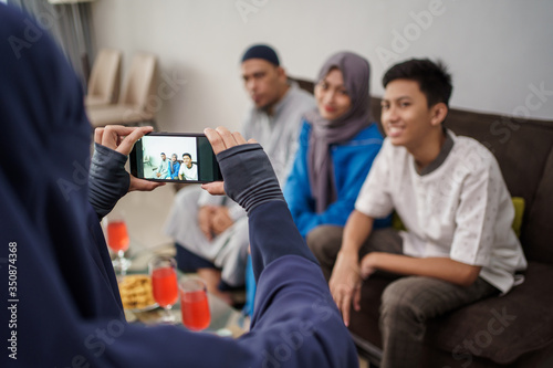 male muslim taking picture of his family while sitting on a couch at home in eid mubarak