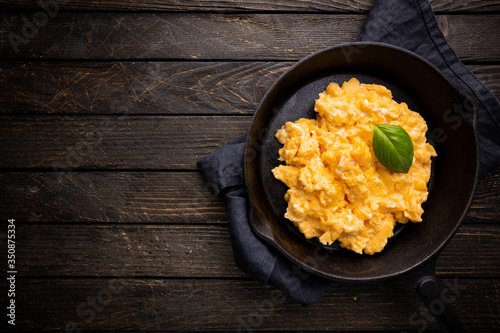 Fresh cooked scrambled eggs in a cast iron skillet on dark wooden background, top view photo