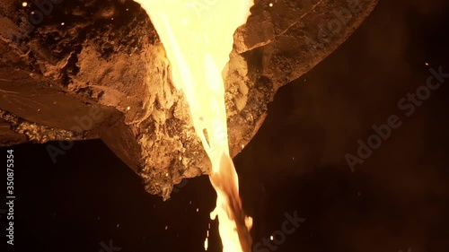 Stream of molten metal poured from one ladle to another in foundry. Liquid metal in metal furnace. Liquid metal production process. Molding molten metal at industrial plant. Slow motion