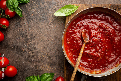 Konstfotografi Classic homemade Italian tomato sauce with basil for pasta and pizza in the pan on a wooden chopping board on brown background, top view