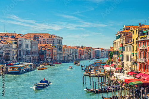 Venice cityscape with Grand Canal waterway. View from Rialto Bridge. Gondolas, boats, vaporettos docked and sailing Canal Grande. Venetian architecture colorful buildings. Veneto Region, Italy.