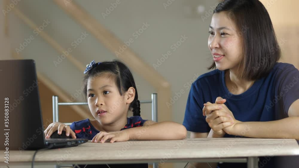 Happy young Asian mom and little ethnic daughter learning online class at home watch video on modern laptop, mother or nanny relax in house with small biracial girl child using computer Happy young Asian mom and little ethnic daughter learning online class at home watch video on modern laptop, mother or nanny relax in house with small biracial girl child using computer