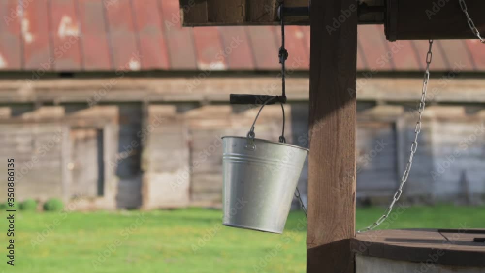 Authentic, traditional well with steel bucket hanging in the wind. Rural farmstead with old barn in background. Authentic, traditional well with steel bucket hanging in the wind. Rural farmstead with old barn in background.