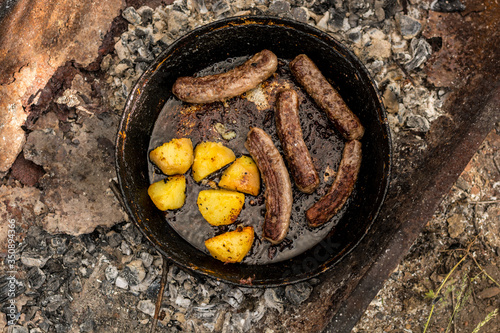 barbecue grill with meat sausages and potato on coals