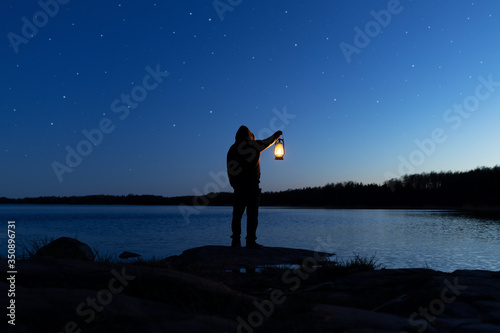 Man holding the old lamp outdoors near the lake. Hand holds a large lamp in the dark. Ancient lantern illuminates the way on a night. Light and hope concept. photo