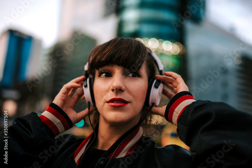 Canvas-taulu Beautiful spanish woman listening to music with earphones and smart phone outdoo