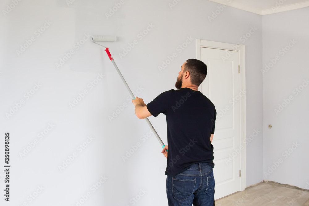 A man paints a wall in an apartment with a roller. Repair in the apartment. A man paints a wall in an apartment with a roller. Repair in the apartment.