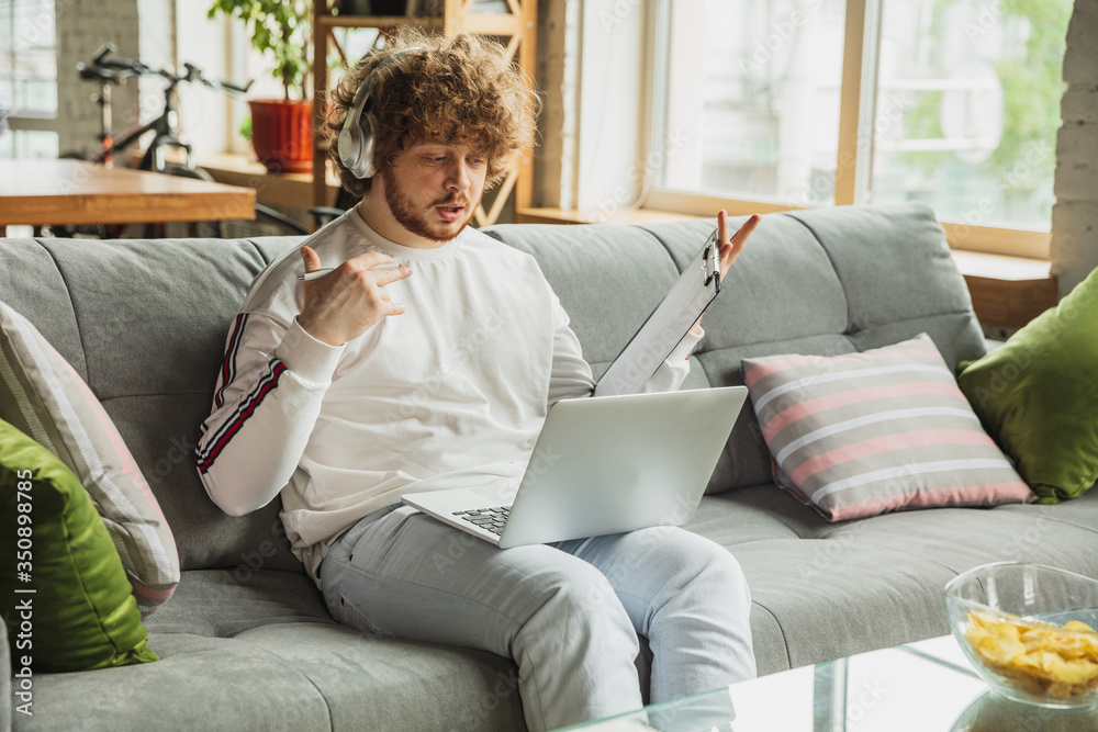 Businessman or student working from home being isolated or keep quarantine 'cause of coronavirus. Caucasian man using laptop, tablet, phone and headphones. Online conference, lesson, remote office.