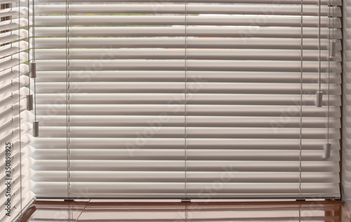 Aluminum blinds. Made from metal. Venetian blinds closeup on the window. Silver color. Closed horizontal blinds in sunny day. Modern sun protection and window decoration.