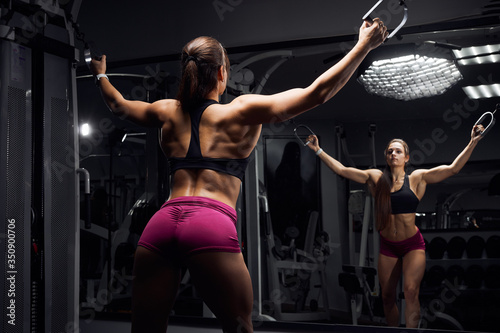 Fitness girl workout in the gym on the simulator, makes spreading exercises with her hands. Sports motivation concept.