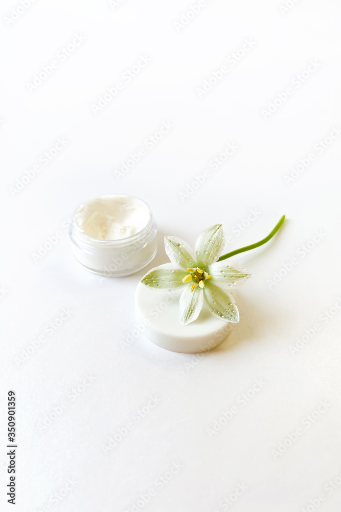 Ornithogalum flower laying on the top of white cap. Open cosmetic jar with white cream. White background. Fresh rain drops. Perfect moisturizer advert.