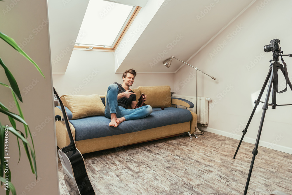 handsome vlogger pointing with finger while knitting on sofa at home in attic room handsome vlogger pointing with finger while knitting on sofa at home in attic room